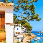 Wooden door of a white house decorated with flowers and view of beach in Sa Tuna fishing village, Costa Brava, Catalonia, Spain